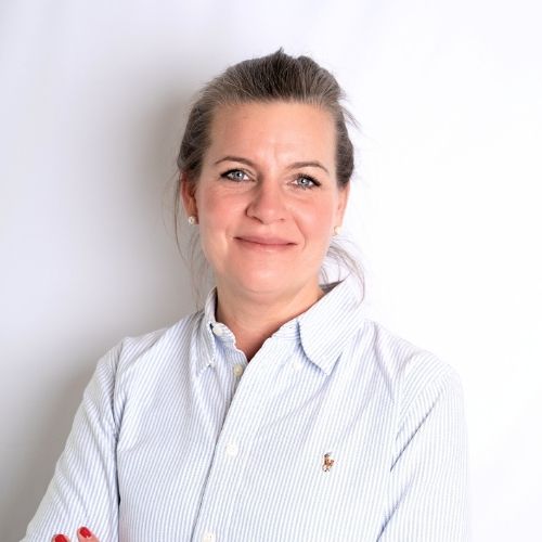 Frau mit blonden Haaren und blauer Bluse, die vor einem weißen Hintergrund lächelt.