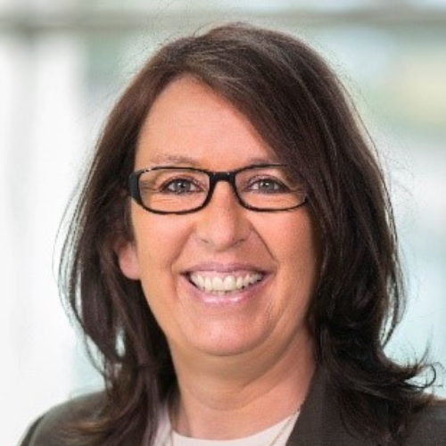 Frau mit langen, dunklen Haaren und Brille lächelt in die Kamera.