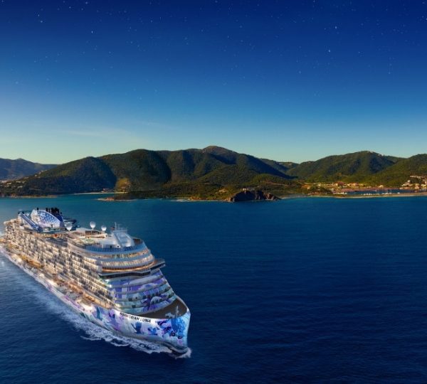 NCL Luna Kreuzfahrtschiff fährt in der Karibik mit grünen Hügeln im Hintergrund.