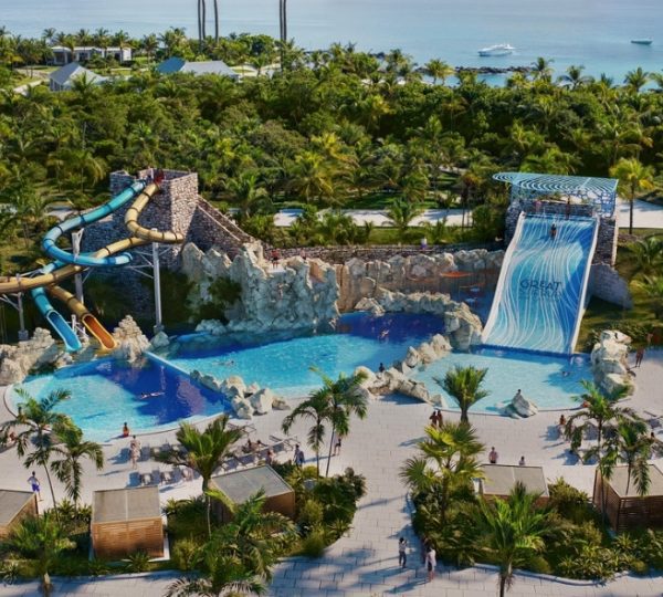 Aussicht auf einen Wasserpark mit Rutschen, einem Wasserfall und einem Poolbereich umgeben von Palmen.