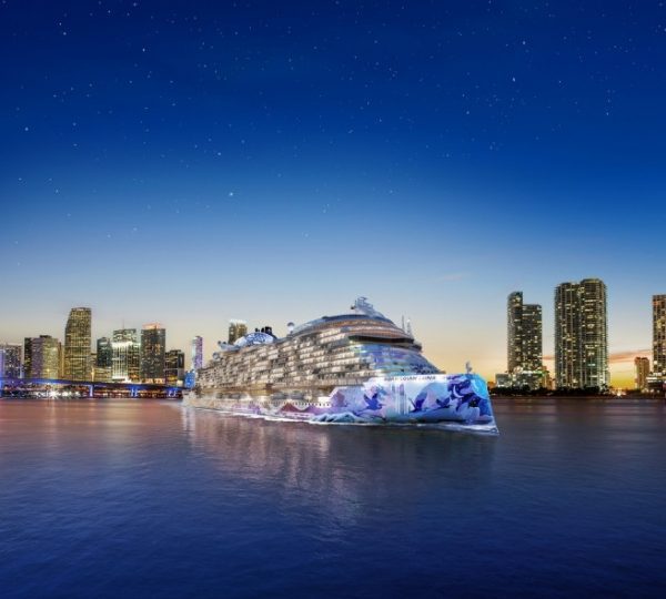 NCL Luna Kreuzfahrtschiff, das vor einer Stadtlandschaft bei Sonnenuntergang im Wasser liegt.