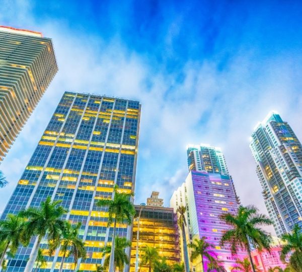 Hochhäuser in Miami mit beleuchteten Fenstern unter einem blauen Himmel.