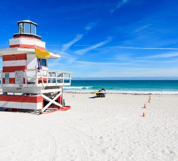 Ein roter und weißer Rettungsturm steht am Strand mit klarem Himmel und Meer im Hintergrund.