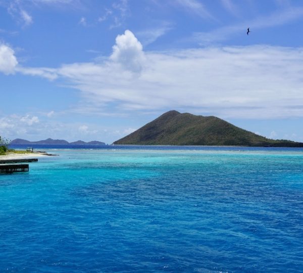 Blick auf das klare Wasser und den Hügel in der Karibik unter einem blauen Himmel.